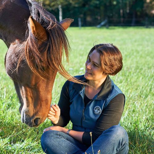 Frau sitzt mit Pferd auf Wiese