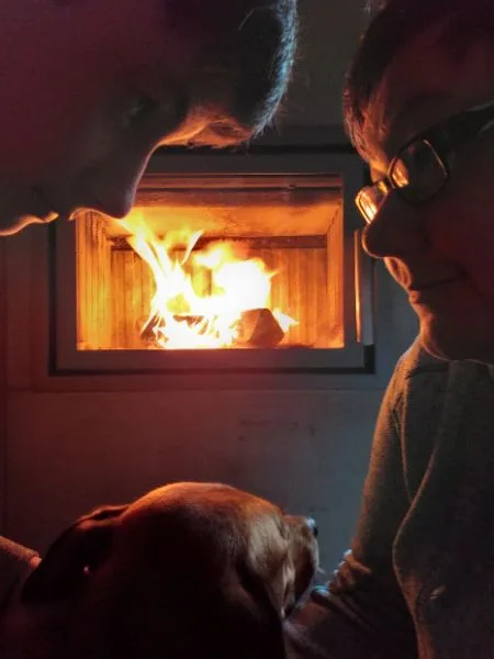 Zwei Menschen schauen vorm Kamin einen Hund an.