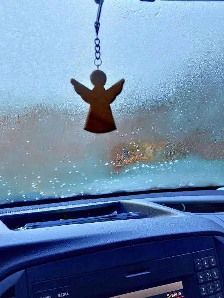 Ein hölzerner Engel hängt an einer Kette an dem Rückspiegel eines Autos.