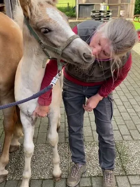 Eine Frau küsst ein helles Fohlen.