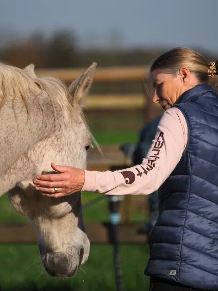 Eine Frau mit blauer Weste berührt ein weißes Pferd am Kopf.