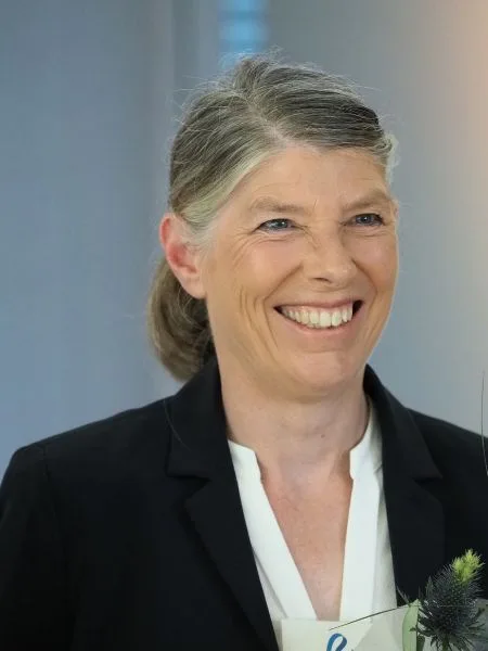 Eine Frau in dunklem Jackett und weißer Bluse strahlt in die Kamera.