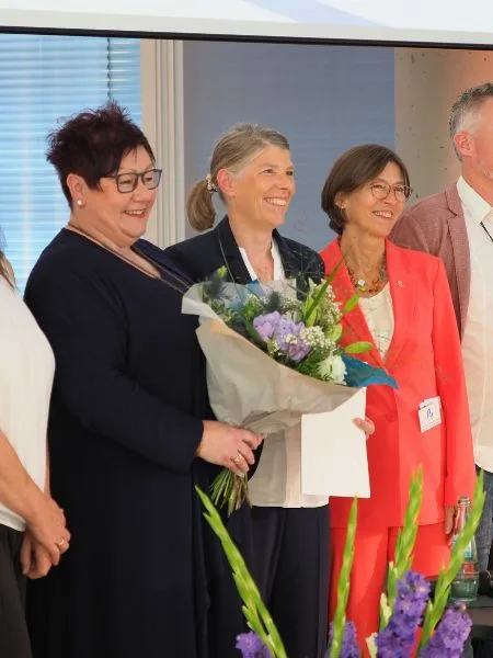 Eine Menschengruppe hält Blumen und lächelt den Fotografen an.