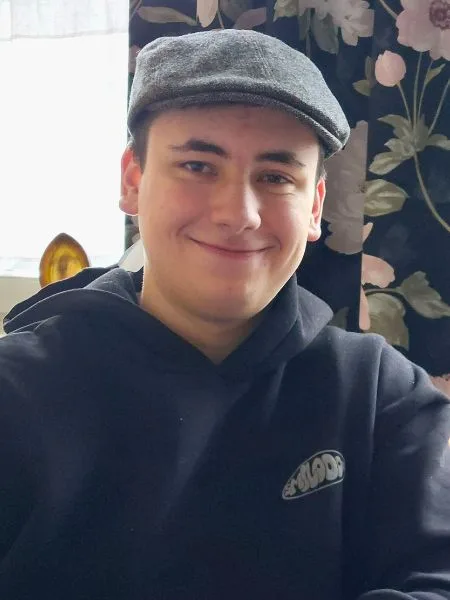 Ein junger Mann mit Basecap und schwarzem Pullover grinst in die Kamera.