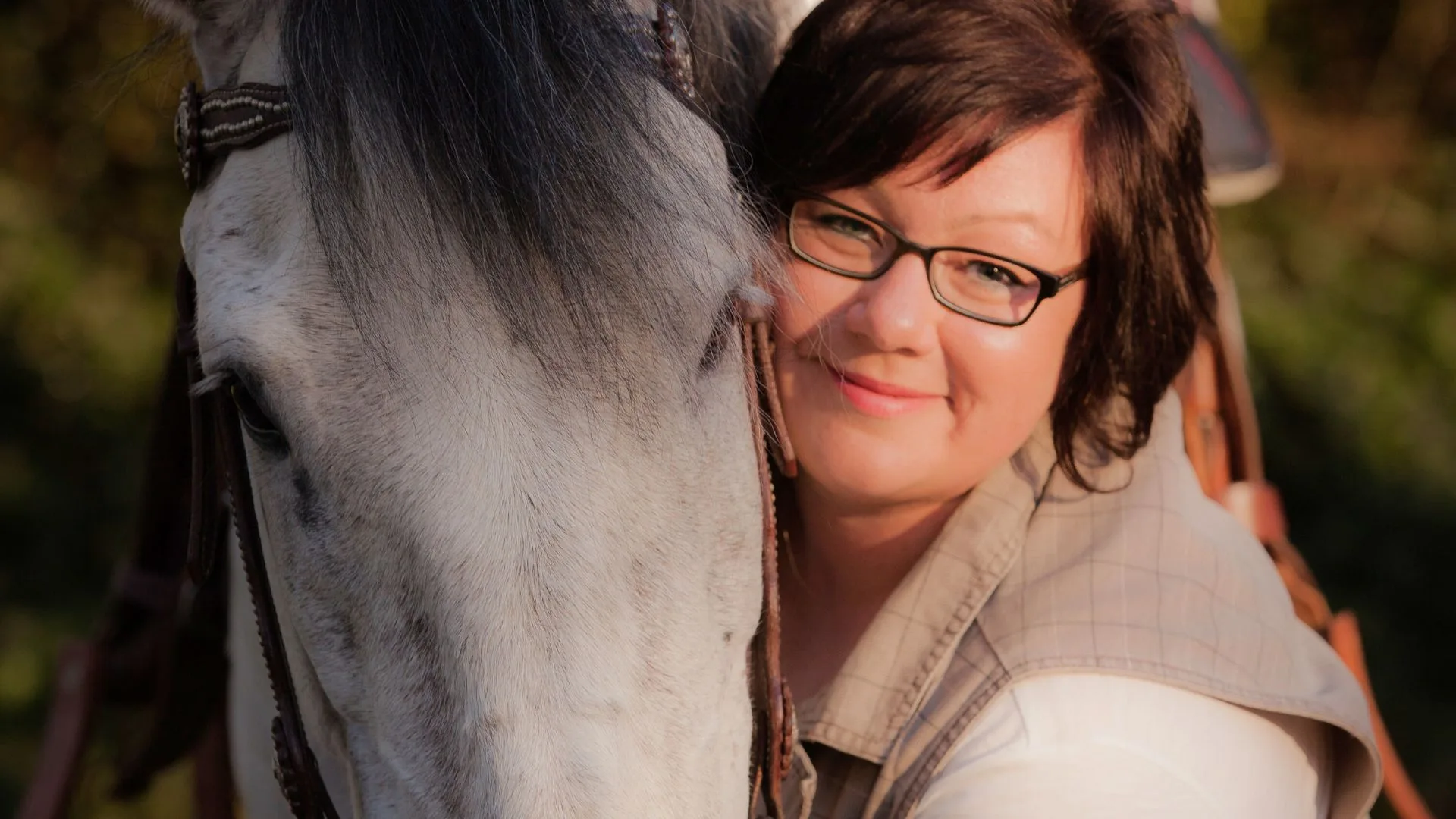 Frau posiert neben weißem Pferd für ein Foto.
