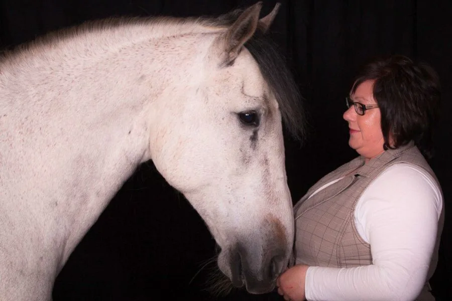 Eine Frau und ein Schimmel sehen sich vor schwarzem Hintergrund in die Augen.