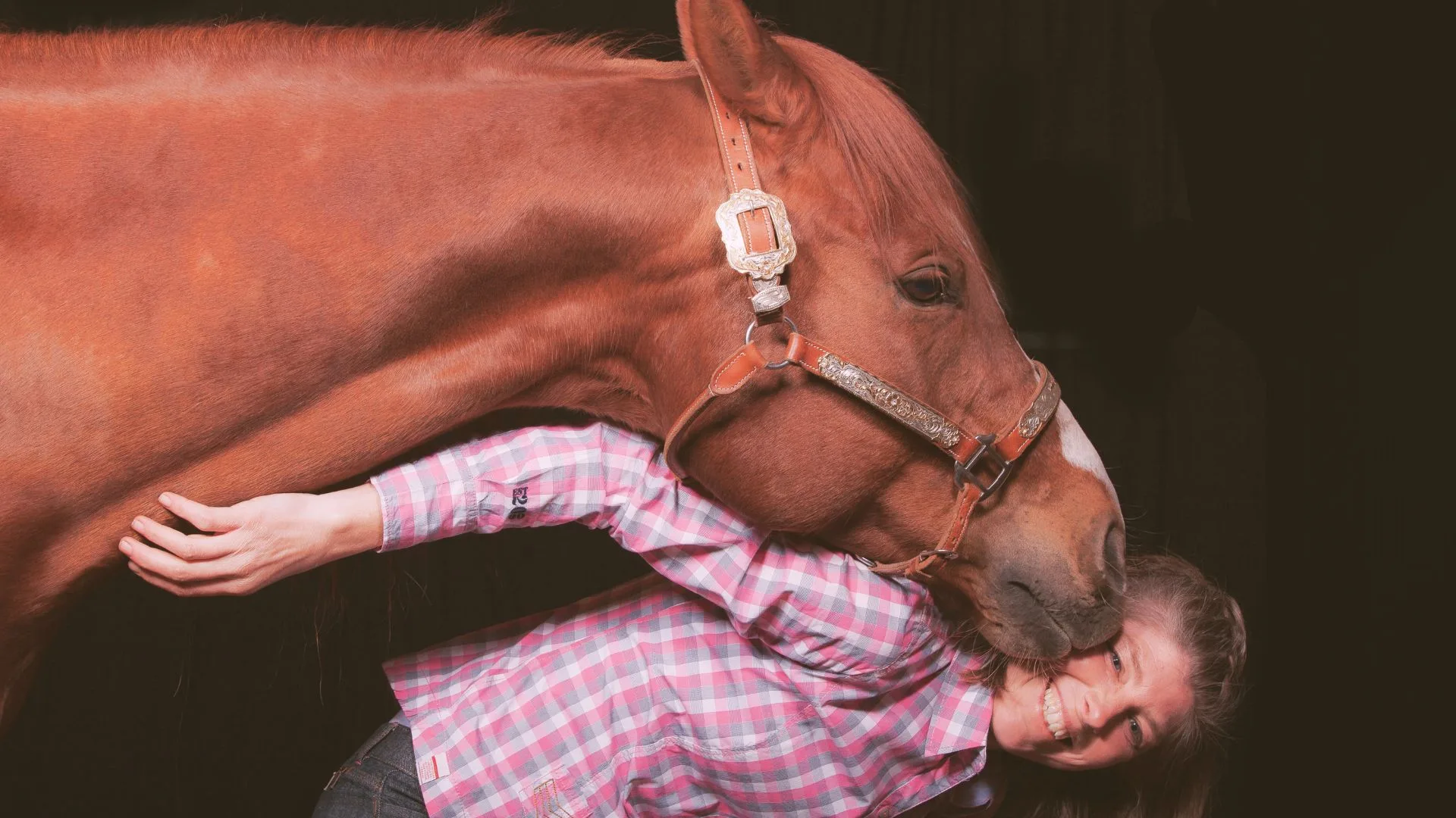 Frau in karierter Bluse posiert neben fuchsfarbenem Quarterhorse.