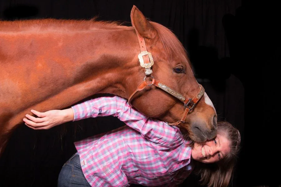 Frau in karierter Bluse posiert neben fuchsfarbenem Quarterhorse.