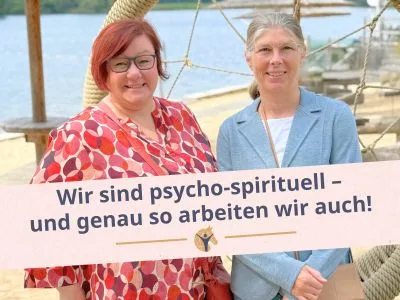 Bloggrafik: Wir sind psycho-spirituell. Zwei Frauen stehen vor einem See und schauen in die Kamera.