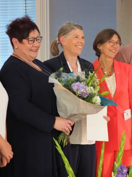 3 Frauen bei einer Preisverleihung mit einem Blumenstrauß in der Hand.