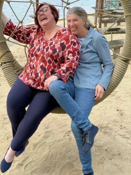 Zwei Frauen sitzen auf einer Netzschaukel am Strand.