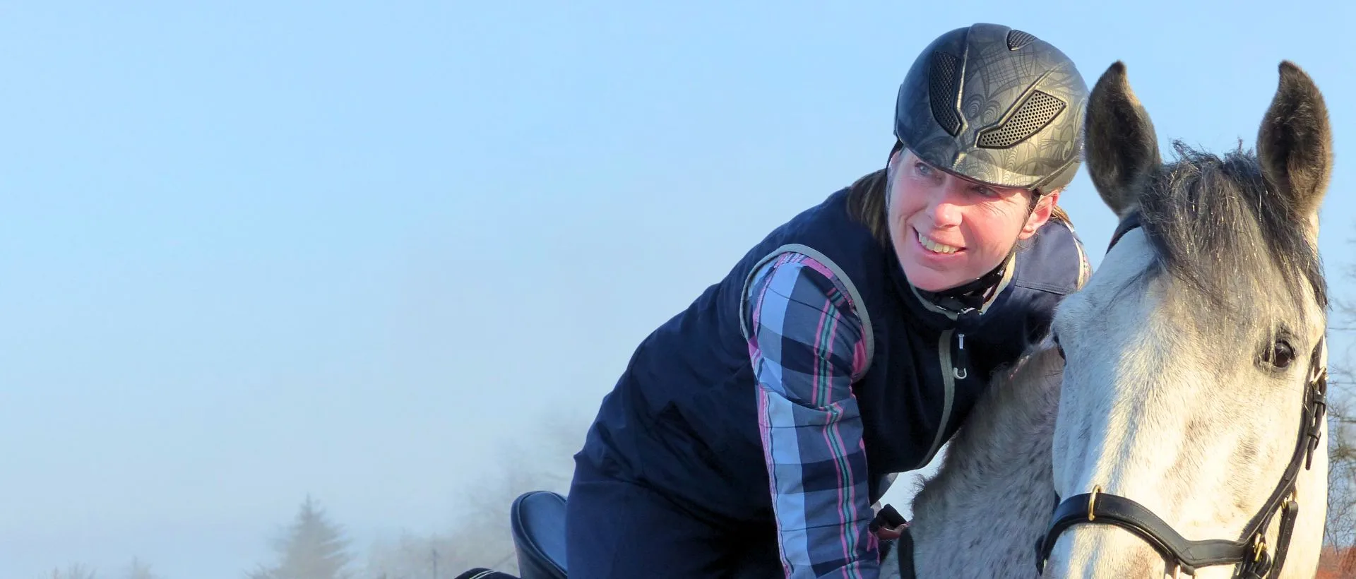 Angstfrei Reiten in einem Tag: Eine blaugekleidete Frau sitzt lächelnd auf einem weißen Pferd.