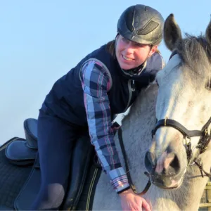 Angstfrei Reiten in einem Tag: Eine blaugekleidete Frau sitzt lächelnd auf einem weißen Pferd.