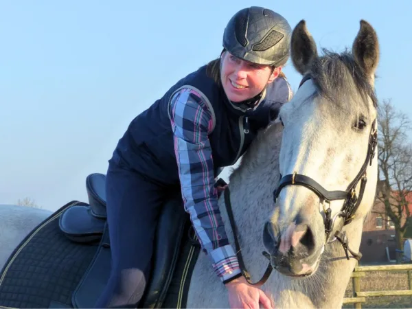 Angstfrei Reiten in einem Tag: Eine blaugekleidete Frau sitzt lächelnd auf einem weißen Pferd.