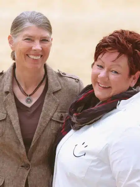 Jutta und Denise Beckmann stehen auf dem Reitplatz und lächeln in die Kamera