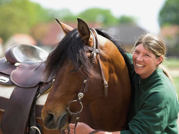 Jutta Beckmann lacht und umarmt ihr braunes Pferd im Westernsattel – Pferdetrainerin vor ihrer Rheuma-Diagnose