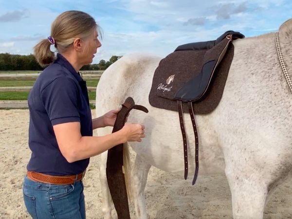 Jutta Beckmann sattelt ihren Schimmel mit einem Filzsattel – Leben mit Rheuma als Pferdetrainerin